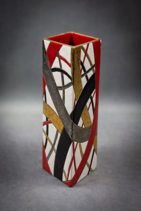 Vase losange "Montagnes Russes" de Catherine Lhoir en Émaux de Longwy. Filets rouges, noirs, or et platine entrelacés sur fond blanc. Vue de trois quart, format portrait.