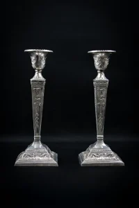 Paire de bougeoirs néoclassiques en métal argenté, ornée de têtes de bélier et nœuds, vue de face