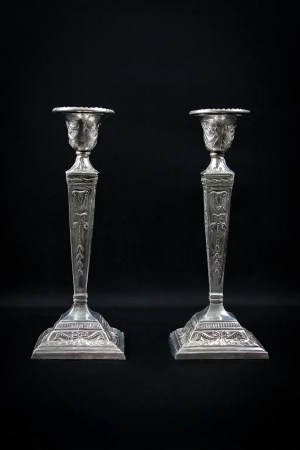 Paire de bougeoirs néoclassiques en métal argenté, ornée de têtes de bélier et nœuds, vue de face