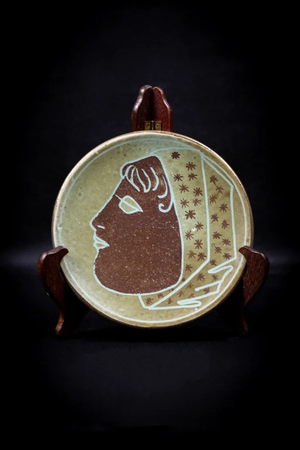 Assiette Accolay au décor de visage féminin stylisé, présentée sur chevalet en bois