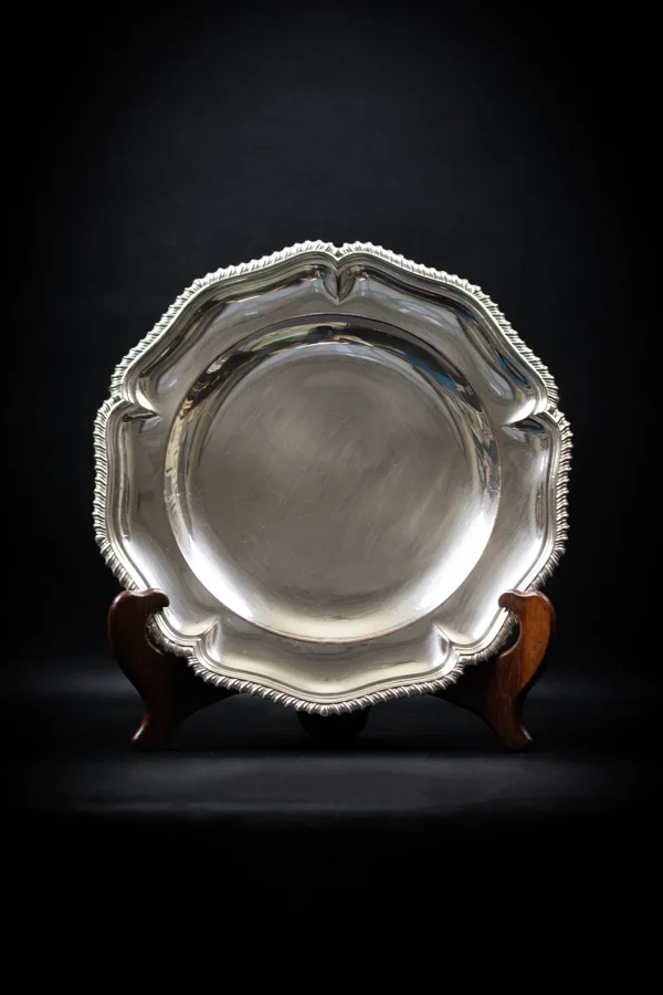 Plat rond en métal argenté à bord chantourné, vue frontale sur support bois