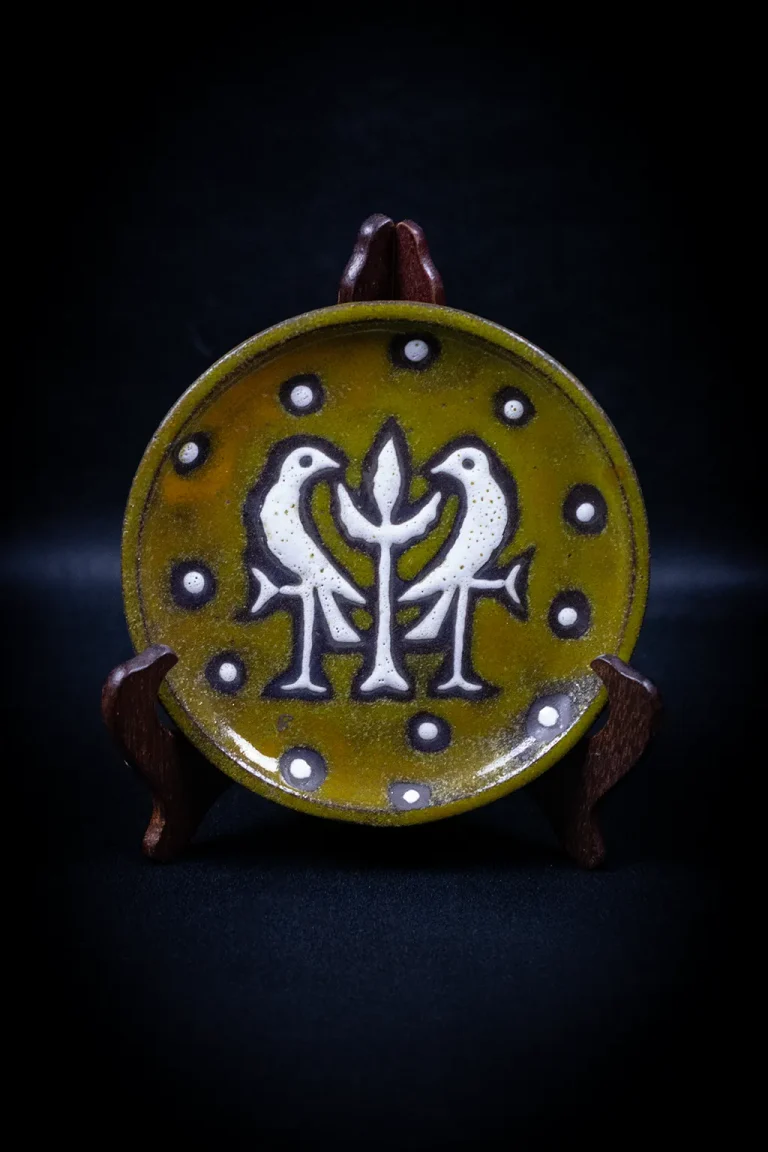 Assiette céramique Rois de Majorque Perpignan, face, fond jaune-olivâtre, deux oiseaux blancs affrontés, arbre stylisé central, présentée sur chevalet